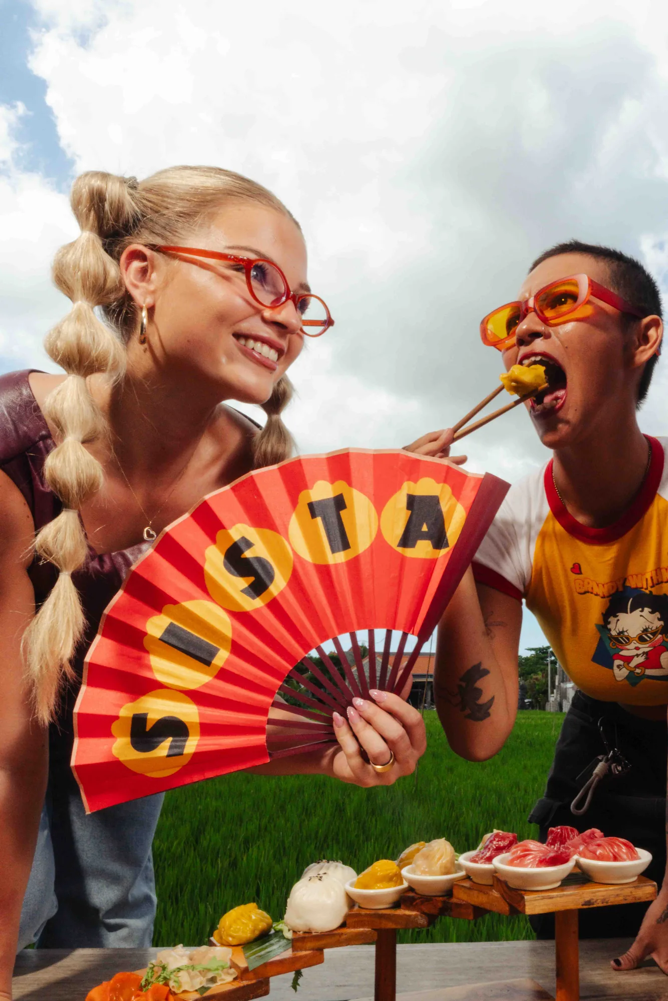 Two friends sharing dumplings, one holding a Sista fan