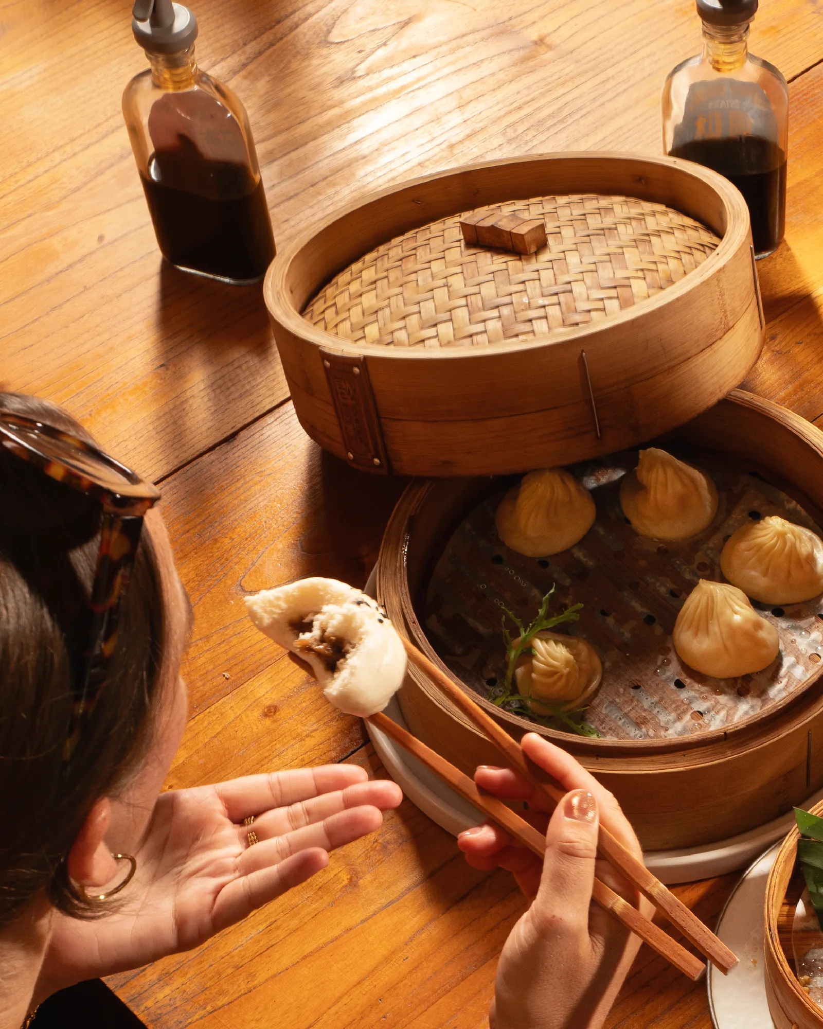 Hands reaching for dumplings from an open bamboo steamer