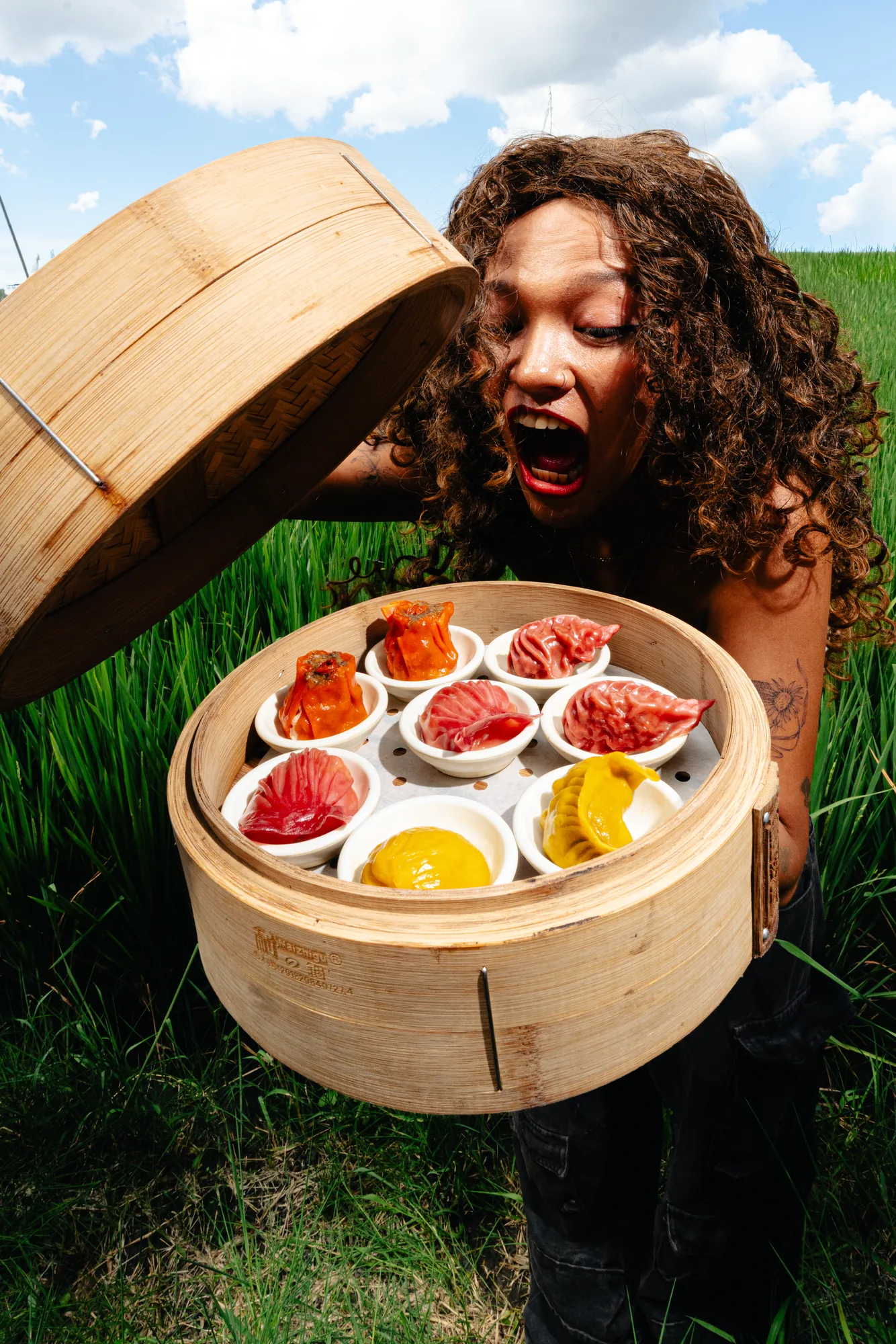 Guest holding an open bamboo steamer filled with colorful dumplings
