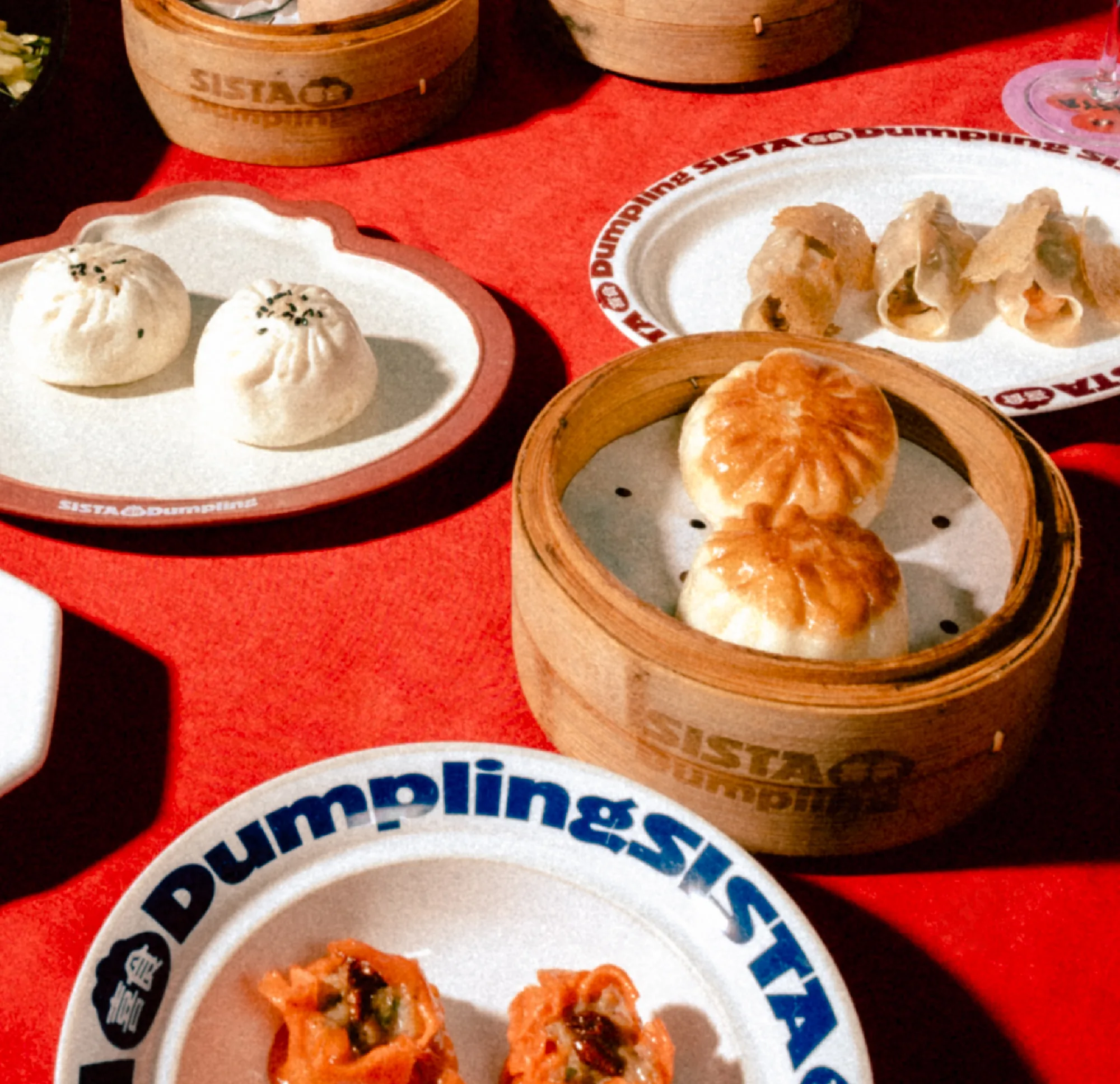 Steamed dumplings served in bamboo steamers and on plates, on a red tablecloth